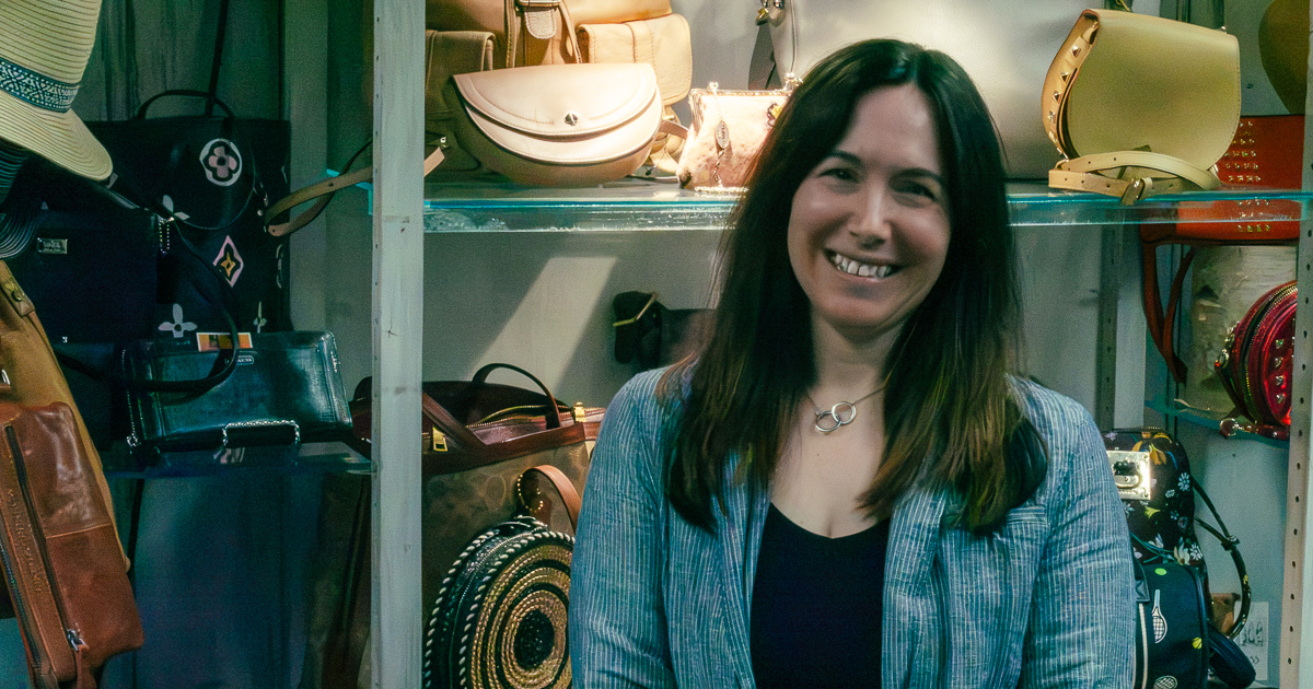 Karen smiling inside Bliss Marketplace with handbags displayed behind her.