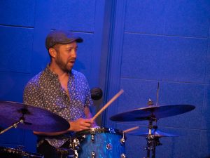 Richie Barshaw plays a blue drum kit under blue stage lighting at The River Room.